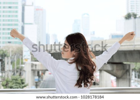 Successful young Asian business woman raising hands at urban building city background.