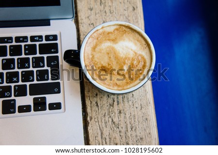 Black cup of coffee on a wooden table with laptop
