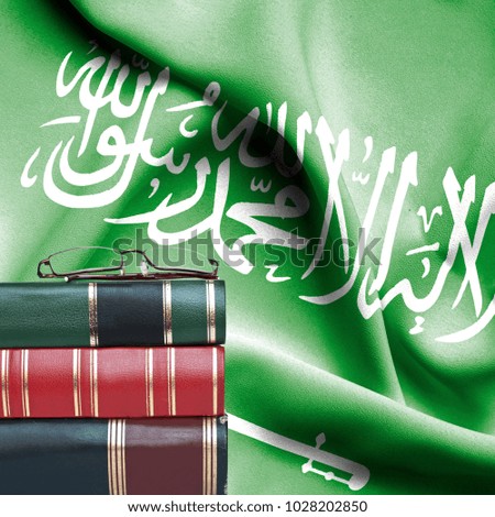 Education concept - Stack of books and reading glasses against National flag of Saudi Arabia