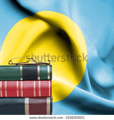 Education concept - Stack of books and reading glasses against National flag of Palau