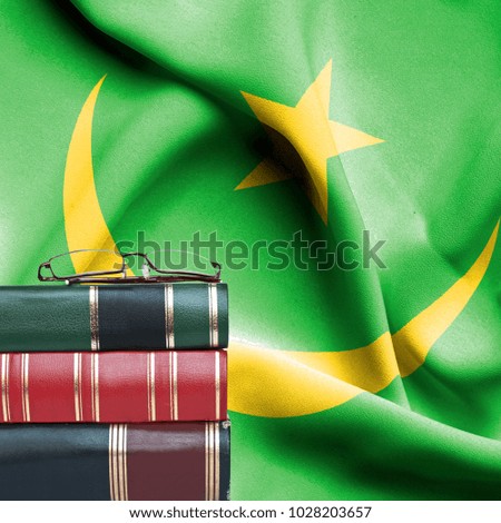 Education concept - Stack of books and reading glasses against National flag of Mauritania