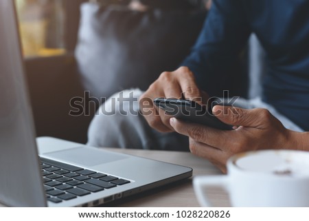 Close up of casual man or freelancer working on laptop computer and holding mobile smart phone with cup of coffee on table in coffee shop or cafe, working from cafe, freelance working concept. Royalty-Free Stock Photo #1028220826
