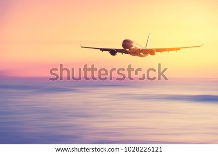 Airplane flying over blur tropical beach with smooth wave and sunset sky abstract background. Copy space of business summer vacation and travel adventure concept. Vintage tone filter effect color.