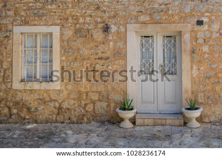 Two flower pots in front of the traditional house in the old city, Budva, Montenegro. Old style house look with stone walls and wooden window and door.  Royalty-Free Stock Photo #1028236174