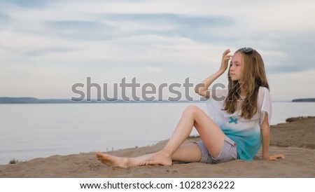 One beautiful teenage girl with brown hair outside on a beautiful summer day. The woman is sitting on the beach. The sun was gone in the sunset.
