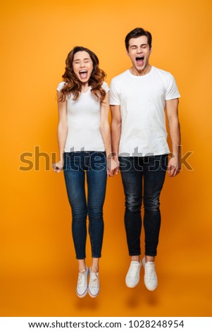 Full-length image of funny man and woman in casual posing on camera with closed eyes while jumping and screaming isolated over yellow background