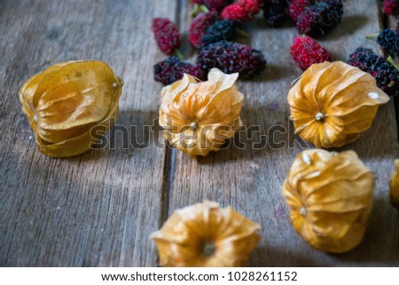 Cape gooseberries and mulberries on the rustic wooden background.