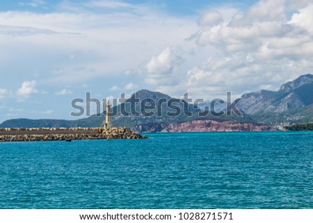The lighthouse in the Bar Marina, Montenegro, Adriatic Sea. Landscape of the coast with the mountains and clouds.  Royalty-Free Stock Photo #1028271571
