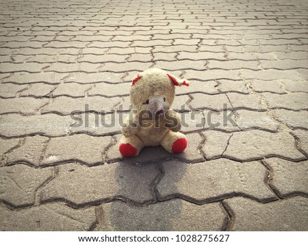 A closeup of an old dirty teddy bear with red feet is sitting alone on cement floor on a sunny day.