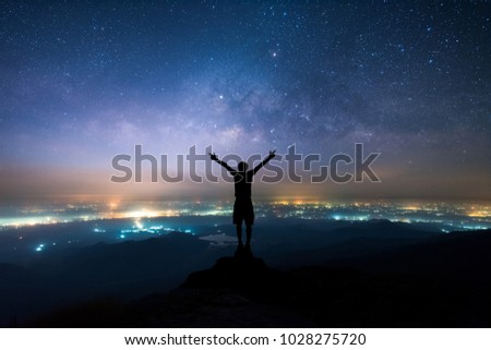 Silhouette of man spreading hand and enjoy to see the Milky Way above the light of countryside area and mountain. Royalty-Free Stock Photo #1028275720