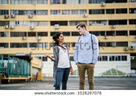 Portrait of a young attractive couple standing and talking together outdoors in the daytime. The female is indian and male caucasian.They are both dressed casually and are laughing.