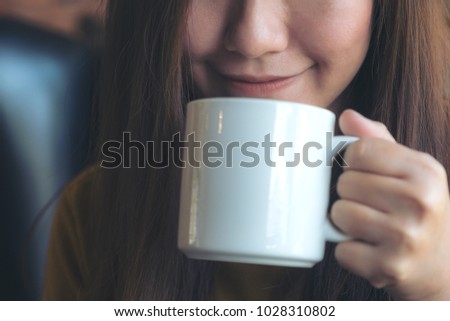 Closeup image of an Asian woman smelling and drinking hot coffee with feeling good in cafe