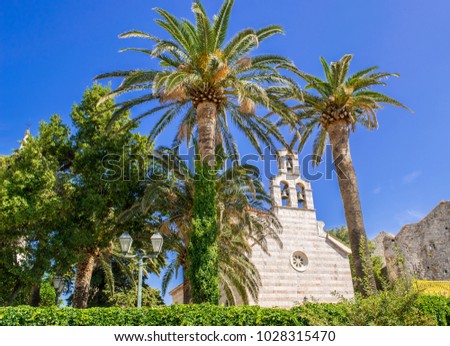 Old church in the old city of Budva, Montenegro, Adriatic Sea. Church building between palm trees.  Royalty-Free Stock Photo #1028315470