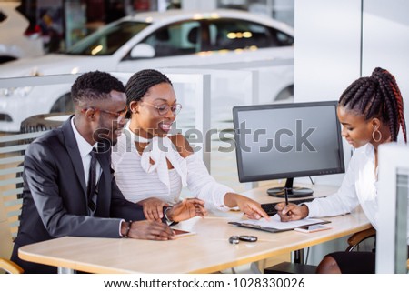 happy African couple and female seller sit at table and make a deal for sale of car