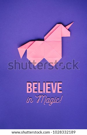 Handmade pink trendy geometrical origami unicorn on ultraviolet background. Believe in magic text, letters, lettering, quote. Vertical poster, postcard, banner.