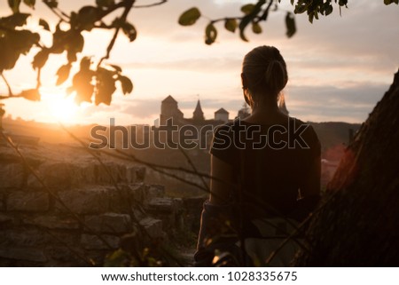 unrecognizable female from the back look at the sunset with a antique castle on the background