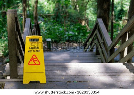 Yellow Caution slippery wet floor sign outdoors near wooden staircase on forest