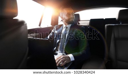 man with laptop sitting in the back seat in the car