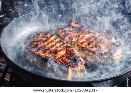 Smoke rises above pork steaks with pepper, salt, garlic and thyme, frying in a grill pan Royalty-Free Stock Photo #1028342317