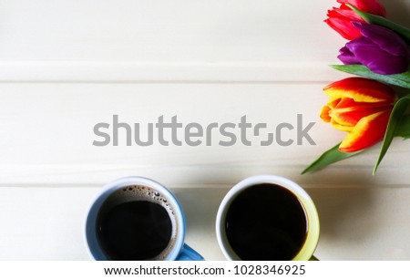 Tulips on wooden background with two cups of coffee. Invitation postcard for mother's day or international women's day. Handmade origami. Punchy pastels. Espresso and americano with flowers