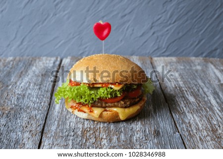 Tasty homemade cheeseburgers with mustard, tomatoes and green lettuce. Sesame burgers with red hearts on wooden background. Food photo with love. Burger on a wooden board