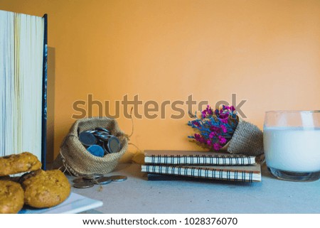 The desk is beautifully decorated with notebooks and dried flowers, along with milk and cookies, and has an orange background to make it more colorful.
