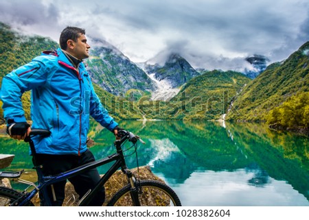 A cyclist stands next to a bicycling on the background an amazing lake and beautiful mountains with fogs. Location: Scandinavian Mountains, Norway. Artistic picture. Beauty world.