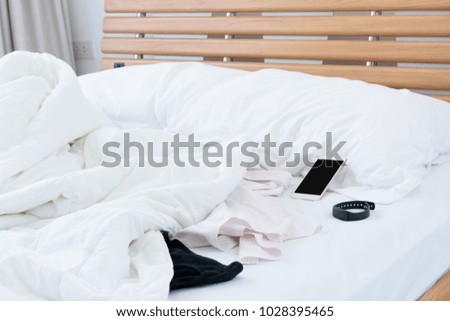 Bedroom interior in morning with smartphone,panty,shirt and fitness wristband on white bedding sheet 
