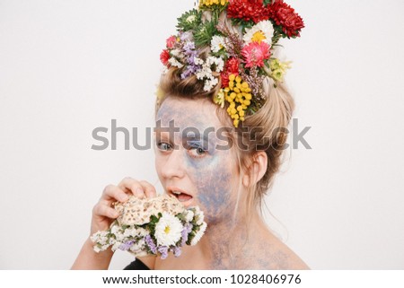 A young woman with flowers on her head and hands. Spring image with flowers. Man with a colorful plant. The girl and the blooming haircuts and brocade on her face.
