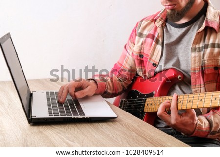 Music college hipster student in checkered plaid shirt practicing electric guitar exercise, reading notes, pc laptop computer. Man teaching himself, taking musical online courses. Background, close up
