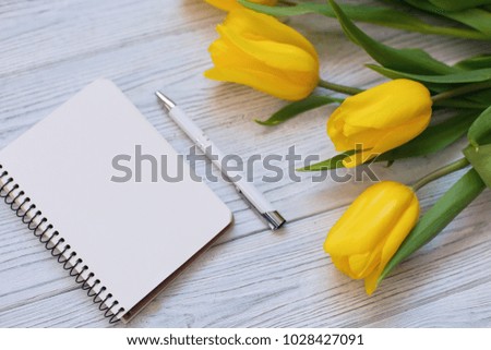 Spring yellow tulips, blank notebook and pen on the white wooden background. Copy space. Flat lay, top view. 