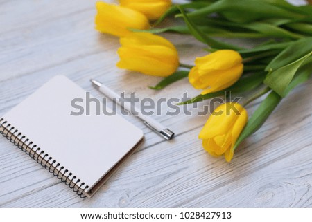 Spring yellow tulips, blank notebook and pen on the white wooden background. Copy space. Flat lay, top view. 