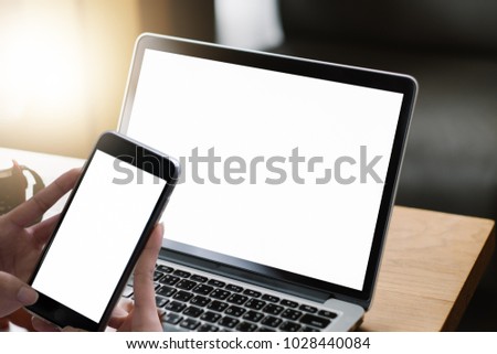 Mockup image of business man using and typing on laptop with blank white screen and coffee cup on glass table in modern loft cafe, Soft focus on vintage wooden table