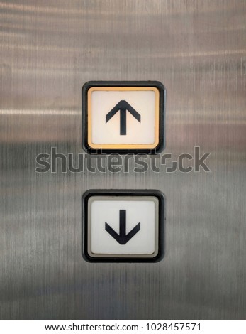 Elevator buttons for up and down with arrows. The buttons are placed on polished stainless steel plate.  Orange light is turned on on the up sign requesting for going upper floor. 