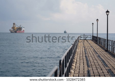Photo of sea with floating cargo ship, wooden pier
