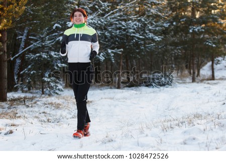 Image of smiling sportswoman in sneakers on morning run against background of trees in winter