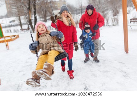 Picture of girl and boy swinging in winter in park with parents
