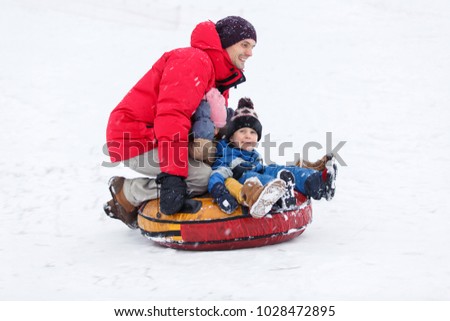 Picture of father, son, daughters riding tubing in winter park
