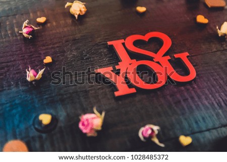 
Red expressive love lettering on a black wooden background and floral decorations of small dried roses and wooden hearts.