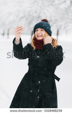 Young caucasian blonde girl in black coat and red knitted scarf walks in winter park