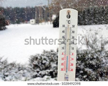Thermometer with Celsius degrees scale in snow on winter country landscape background