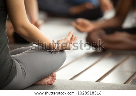 Young sporty woman practicing yoga lesson sitting in Sukhasana exercise, Easy Seat pose with mudra gesture, working out, female arms with wrist bracelets close up, studio Royalty-Free Stock Photo #1028518516