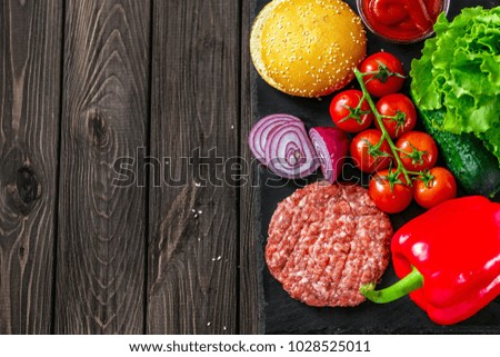From above shot of process of making hamburger with vegetables, buns and raw meat on board.