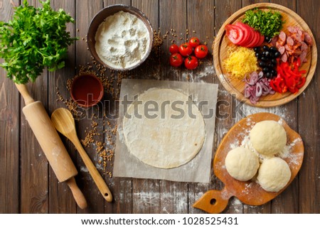 Pizza dough with ingredients on wood, shot from above