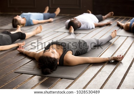 Group of young afro american and caucasian sporty people practicing yoga lesson lying in Dead Body pose, Savasana exercise, working out, resting after practice, indoor close up, studio Royalty-Free Stock Photo #1028530489
