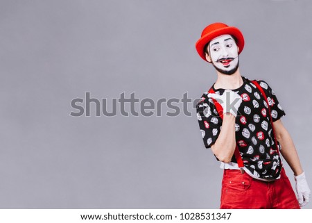 cheerful mime posing near a gray background