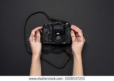 Female hands, vintage camera with a strap on a black background, top view, minimal flat lay background.