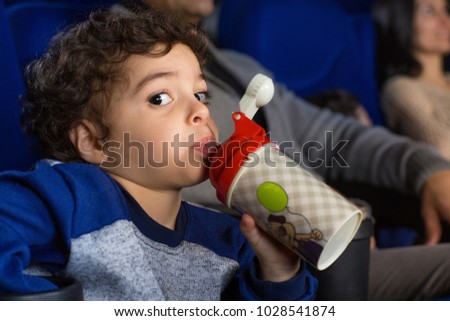Close up of a little adorable boy looking to the camera sipping his drink while enjoying watching a cartoon at the movie theatre copyspace relax drinking beverage kids children entertaining leisure.