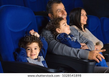Adorable little boy smiling happily to the camera sitting at the cinema with his brother and parents family parenting parenthood childhood happiness kids siblings love children entertainment leisure.