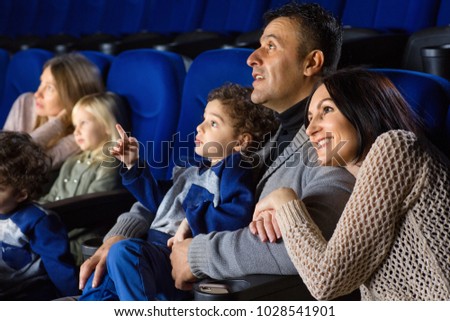 Happy loving family embracing smiling joyfully watching a movie together at the cinema copyspace people lifestyle happiness parents couples love children weekend leisure positive activity.